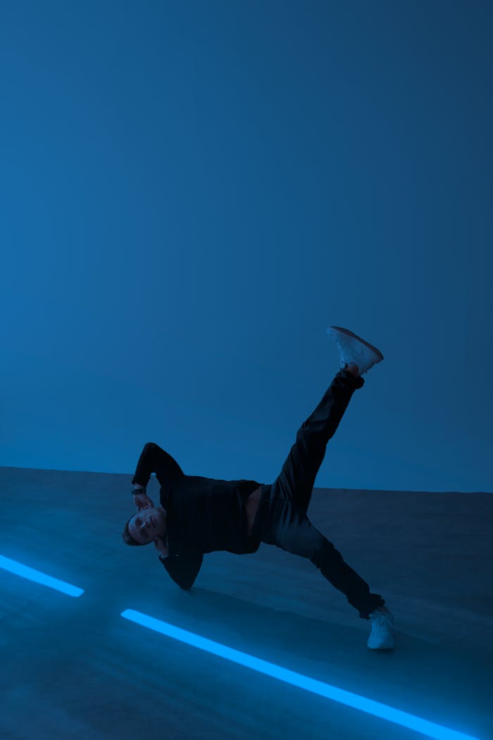 A dancer performs a dynamic pose against a blue neon-lit backdrop, showcasing modern movement.